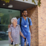 Caregiver walking with senior woman client in front of a nurishing home.