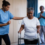 Nurse assisting senior woman in walking with walker at retirement home