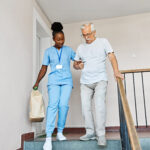 Doctor or nurse caregiver helping disabled senior man walking down the stairs at home or nursing home
